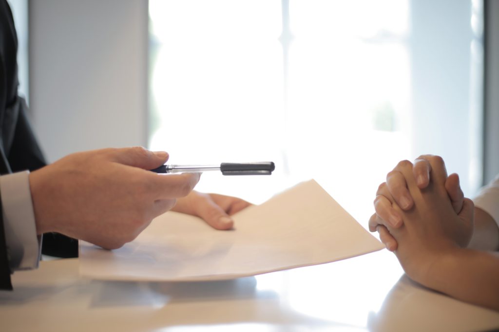 A company representative with paperwork in hand, pointing a pen at a borrower, representing fair HMDA lending practices. 